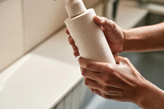 A close-up of hands holding a damp lotion bottle, showcasing the sleek design, perfect for emphasizing skincare products and their importance in daily routines.