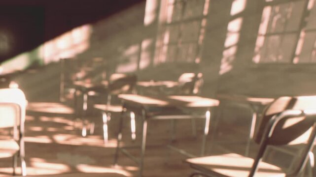 Sunlight illuminates rows of vacant school desks in a quiet classroom during the late afternoon hours.