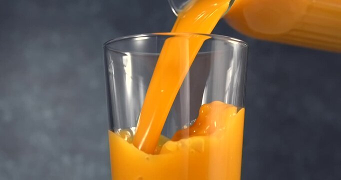 Orange juice pouring into glass in slow motion on black background
