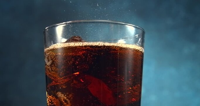 Cola type drink bubbles bursting and spraying from a fresh fizzy drink with ice in slow motion