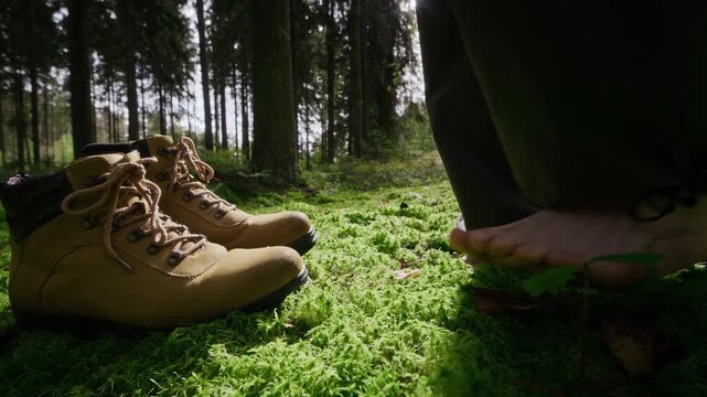 Caucasian traveler stepping barefoot onto green moss next to hiking boots in slow motion. Ideal for mental health campaigns, grounding therapy, and eco-friendly wellness ads