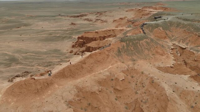 Cinematic drone shot overlooking the sweeping clay hills, deep ravines, and red earth textures of the Flaming Cliffs during an expedition across the Gobi Desert, Mongolia