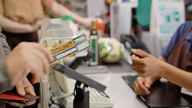 Unrecognizable customer paying with contactless credit card at store checkout terminal and receiving discount coupons. Ideal for retail banking promotions and supermarket loyalty program ads