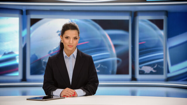 Female News Anchor Seated at a Studio Desk With a Tablet, Looking Into the Camera as She Delivers International Headlines and Current Affairs for a Live Evening Television News Bulletin.