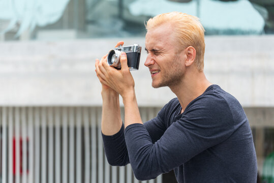 Smiling caucasian man photographer look at photo from professional camera outdoor. Men White People with vintage film camera take a photo. Young man shooting photo in green nature park outdoor travel