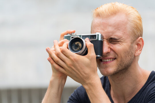 Smiling caucasian man photographer look at photo from professional camera outdoor. Men White People with vintage film camera take a photo. Young man shooting photo in green nature park outdoor travel