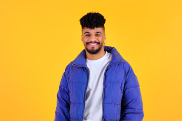 Happy young man smiling wearing blue puffer jacket on yellow background © Cristina Garcia