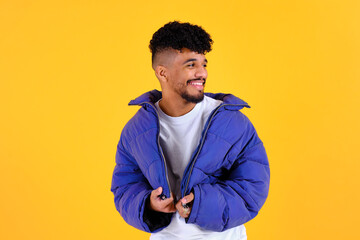 Young man smiling wearing puffer jacket on yellow background © Cristina Garcia