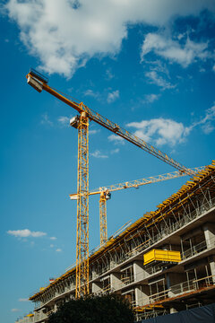 Construction cranes lifting materials on building site against blue sky
