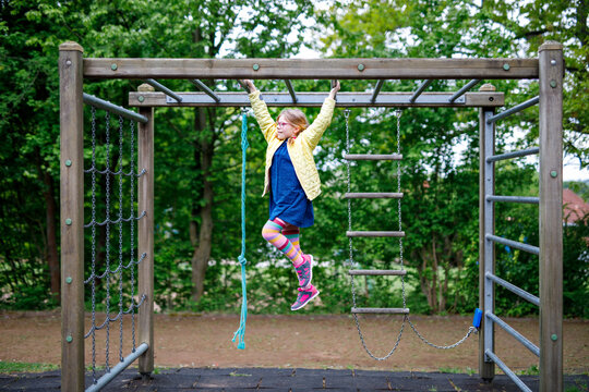 Little girl doing gymnastics on a climbing frame, horizontal bar on school yard. Child enjoying school break.