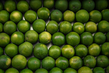 Fresh green limes arranged in dense rows with varied sizes, textured peels, and natural color differences, creating a vibrant overhead produce background with repeating round shapes © I K Photography