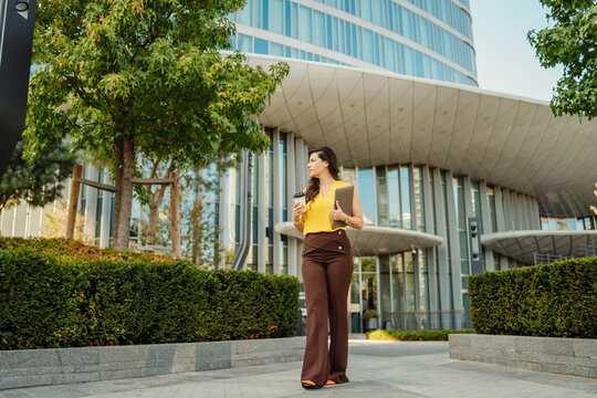 Businesswoman walking in city with coffee and laptop