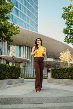 Businesswoman walking with coffee and laptop outside modern office building