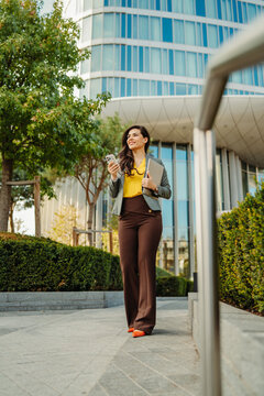Confident businesswoman walking outdoors with phone and laptop