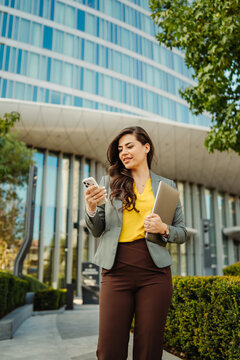 Businesswoman checking smartphone while walking outside office building