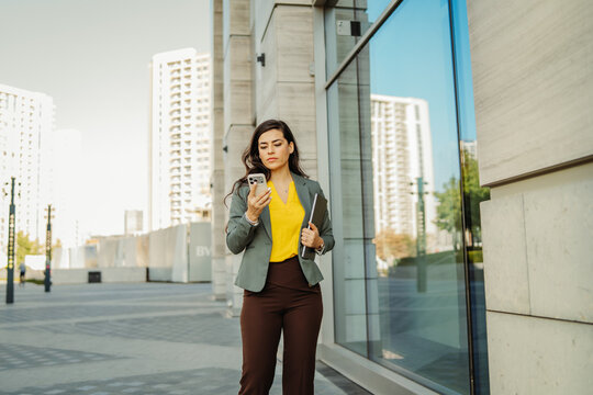 Businesswoman using smartphone walking in modern city street