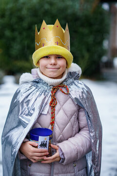 Smiling child dressed as a Sternsinger with crown and silver cape, holding a donation box during the Epiphany tradition in Germany