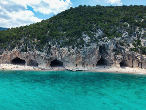 Aerial view of the limestone caves of Cala Luna beach with sunbathers and turquoise sea, Gulf of Orosei, Sardinia, Italy