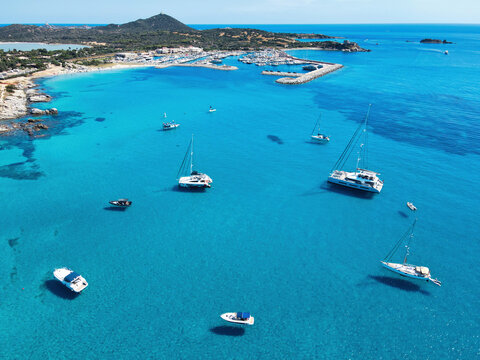 Aerial view of sailboats, catamarans and motorboats anchored in turquoise water near Campulongu beach and the marina, Villasimius, Sardinia, Italy