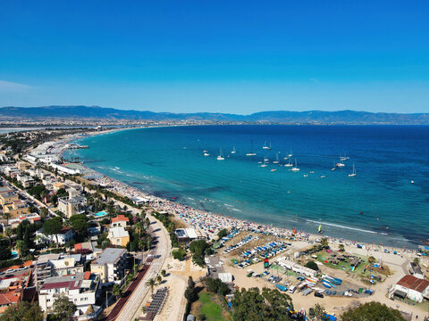 Aerial view of Poetto beach in Cagliari with crowded sandy shore, turquoise sea, sailboats and coastal road, Sardinia, Italy