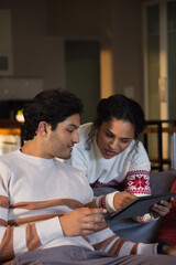 African American couple wearing sweaters on sofa at home, woman pointing tablet, man holding device © WavebreakMediaMicro