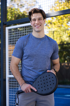 Man standing on fenced racket court holding paddle wearing blue athletic shirt and wristwatch