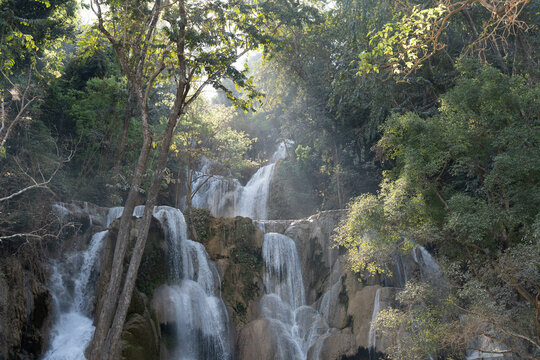 Aerial view of the tiered Kuang Si Waterfall cascading over limestone formations surrounded by lush tropical jungle foliage in Luang Prabang, Luang Prabang Province, Laos.