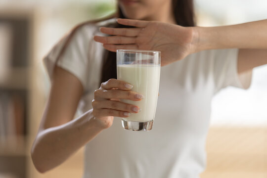 Asian woman refusing glass milk expressing lactose intolerance allergy aversion with hand gesture in indoor kitchen room