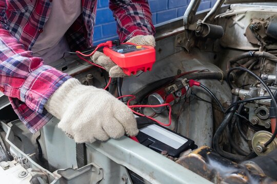 Horizontal stock photo of mechanic measuring car battery voltage with digital multimeter in auto repair shop