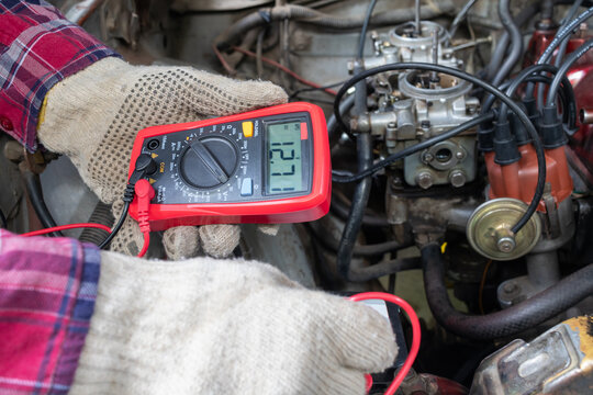 Horizontal stock photo of mechanic checking voltage with digital multimeter in car engine bay