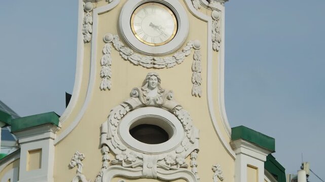 Vintage clock with Roman numerals sits on ornate building facade. Carved female face sculpture decorates classical architectural element