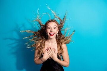Plakat Excited young woman with windblown hair smiling and surprised in a glamorous portrait against a bright blue background