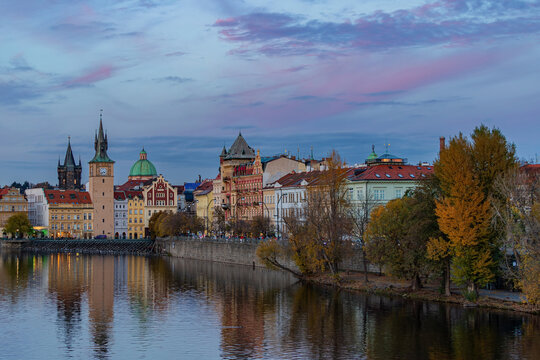 Fall landscape view of Smetanovo embankment (Smetanovo nabrezi) with historical buildings along Vltava river and autumn trees under a cloudy sky. Prague, Czech Republic