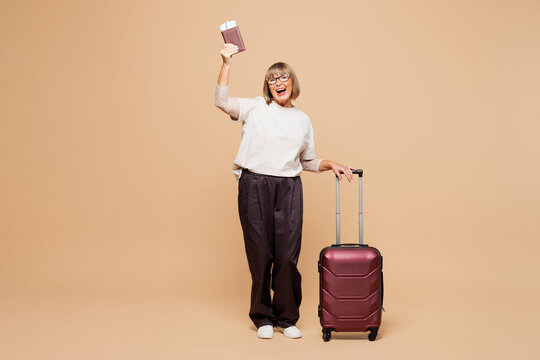 Traveler elderly woman wear casual clothes hold passport ticket bag isolated on plain pastel beige background studio. Tourist travel abroad in free time rest getaway. Air flight trip journey concept.