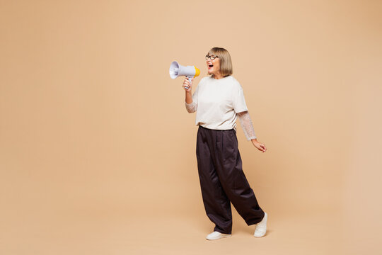 Full body elderly blonde woman 50s years old wear white shirt casual clothes hold megaphone scream announces discounts sale Hurry up isolated on plain pastel light beige background. Lifestyle concept.