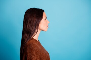 Profile portrait of a thoughtful woman with long brown hair wearing a brown sweater against a bright blue studio background, side view for lifestyle and fashion use © deagreez