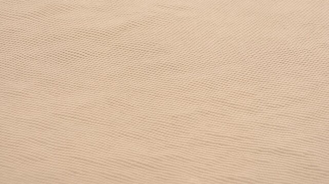 Beige woven fabric surface gently undulates in a soft abstract close-up. Fashion design, textile presentation, and editorial layout.