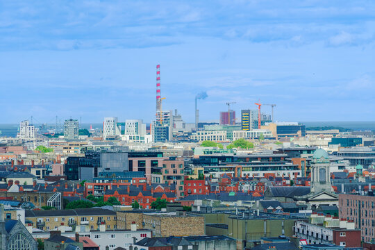 View of the Dublin skyline featuring industrial chimneys, modern office buildings, historic rooftops, and construction cranes under a cloudy sky in Dublin, County Dublin, Ireland.