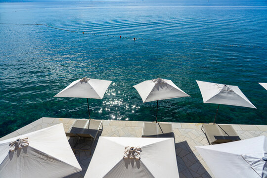 Seaside terrace with umbrellas and loungers overlooking calm blue ocean water Opatija Croatia