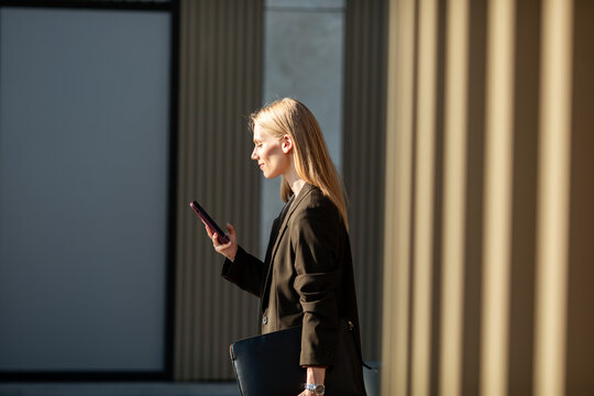 Businesswoman checking smartphone while walking by office columns