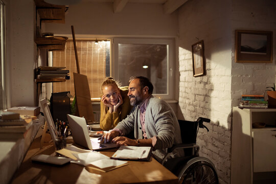 Wheelchair user and woman collaborating on laptop at home
