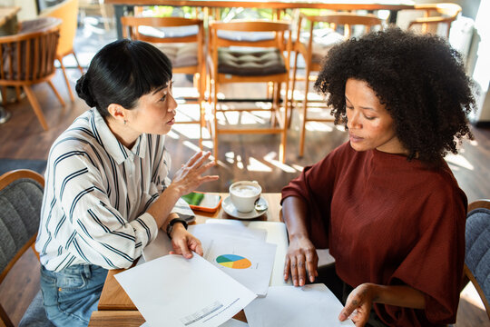 Two women discussing pie chart printouts at a cafe