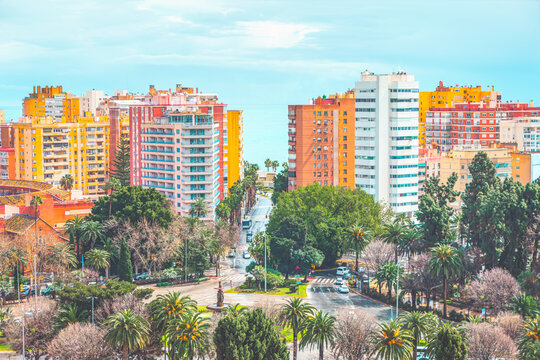 Aerial view of Malaga, Spain, with wide avenue leading toward the Mediterranean Sea. High-rise buildings, palm trees and green urban spaces highlight the city coastal landscape and modern development
