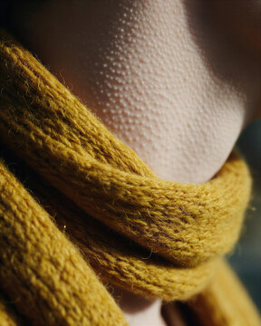 Extreme close-up of goosebumps on skin wrapped in a cozy yellow woolen scarf, highlighting the tactile sensation of human and autumn cold.