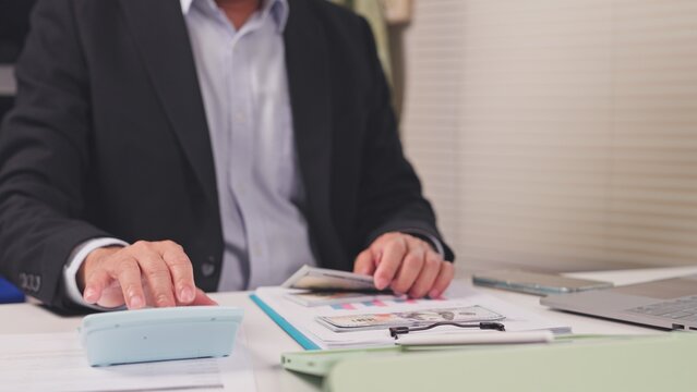 Businessman calculates financial budget, dollar banknotes, paperwork reports at desk. Corporate revenue accounting, investment cash flow audit, loan profit analysis, tax return assessment.