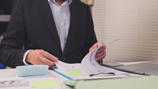Businessman reviews financial report documents beside calculator laptop at workplace. Corporate budget audit, investment revenue analysis, commercial bookkeeping accounting assessment.