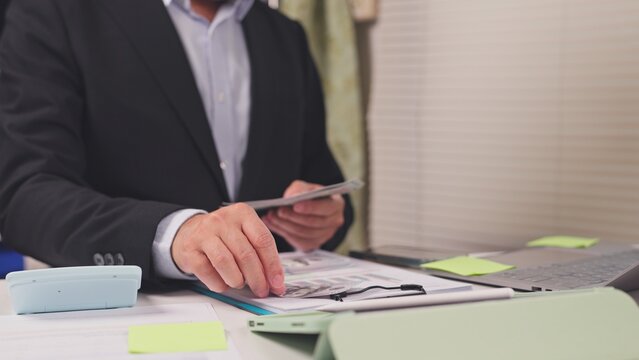 Businessman counts dollar banknotes over financial chart paperwork in office. Corporate cash flow management, revenue accounting audit, commercial budget expense review, currency profit analysis.