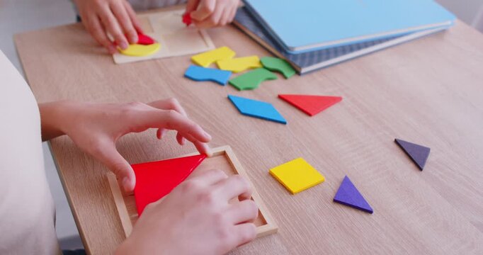 Unrecognizable clever children engaged in team work, joining colourful geometric shapes or mosaic pose at wooden table at home enjoy self development. Family leisure board games and learning concept
