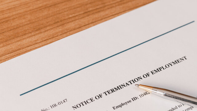 Notice of termination of employment document with a pen on a wooden desk. Job layoff, contract cancellation, workforce reduction, corporate firing, and employment dismissal concept