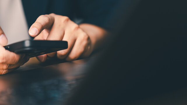 Close-up of person using smartphone and laptop computer at desk. Concept of mobile technology, communication, digital lifestyle and modern business working connection